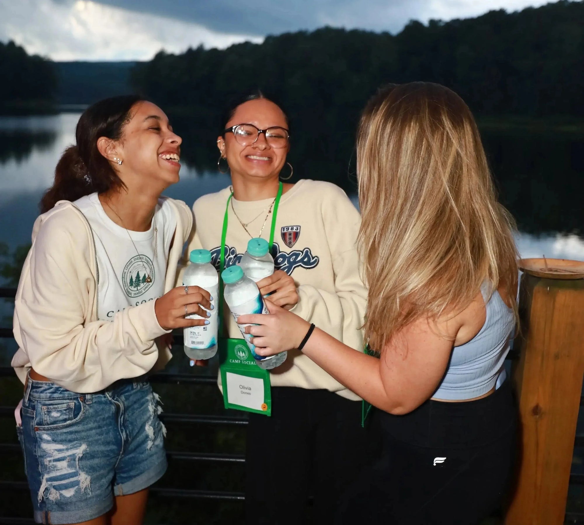 Three women laughing on a lakeside deck at camp